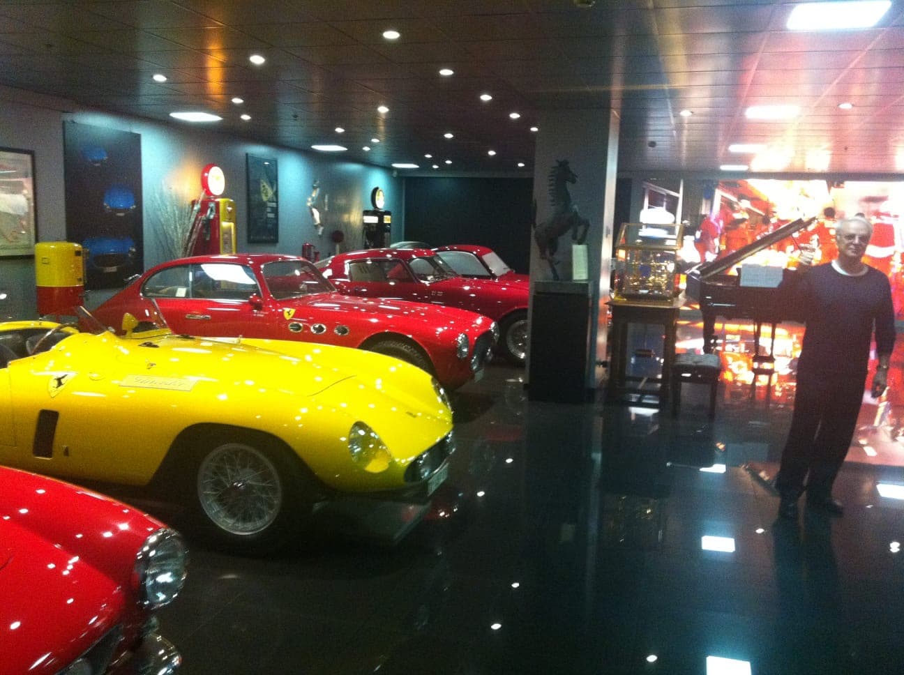 Vintage red and yellow Ferraris in a showroom with a man and a grand piano.