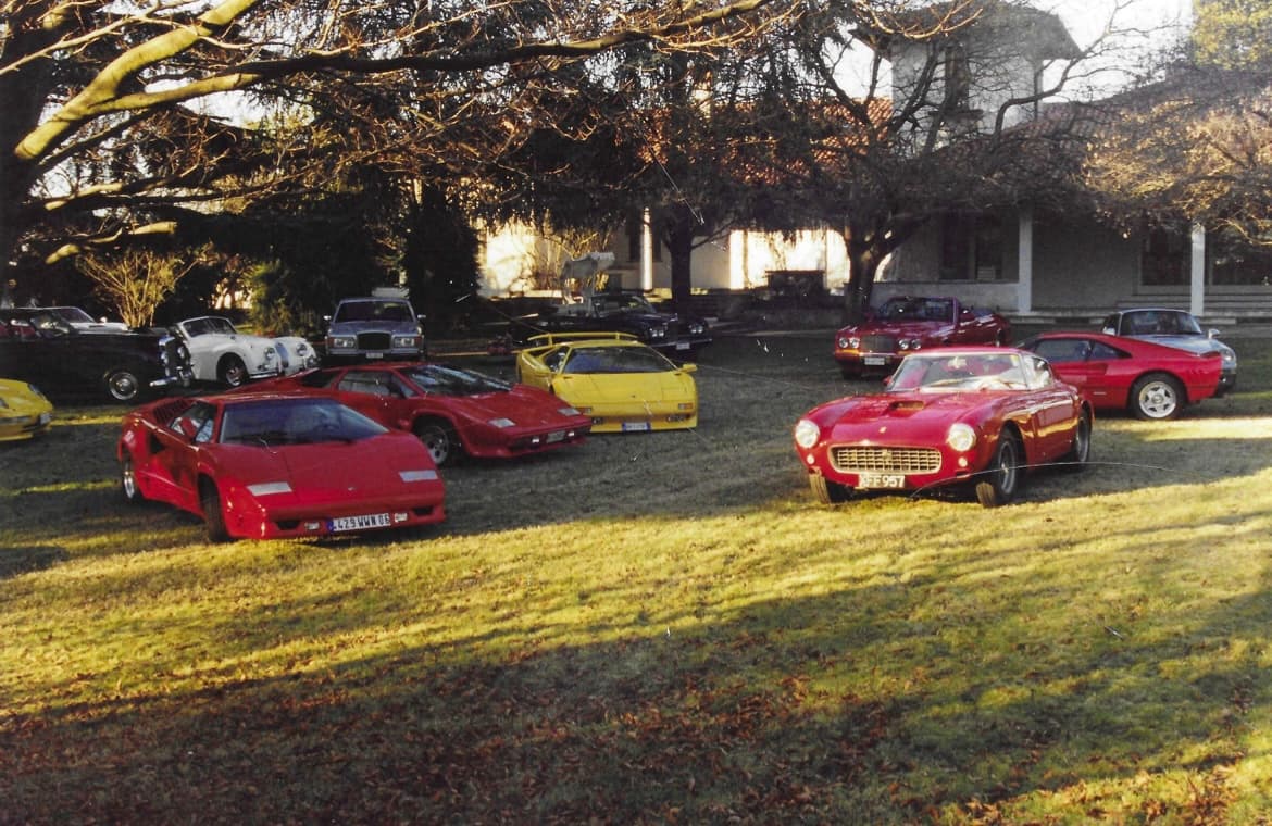 Luxury sports cars, including Ferraris and Lamborghinis, parked on a lawn before an estate.