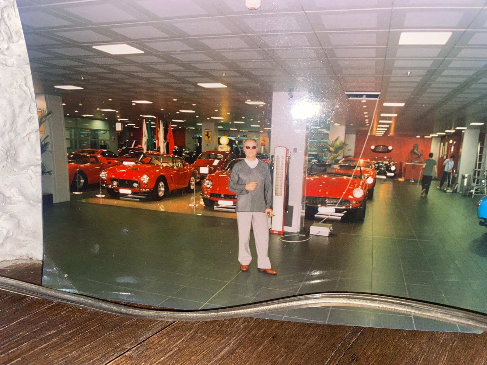 Man in a grey sweater standing among a collection of classic red Ferrari sports cars.