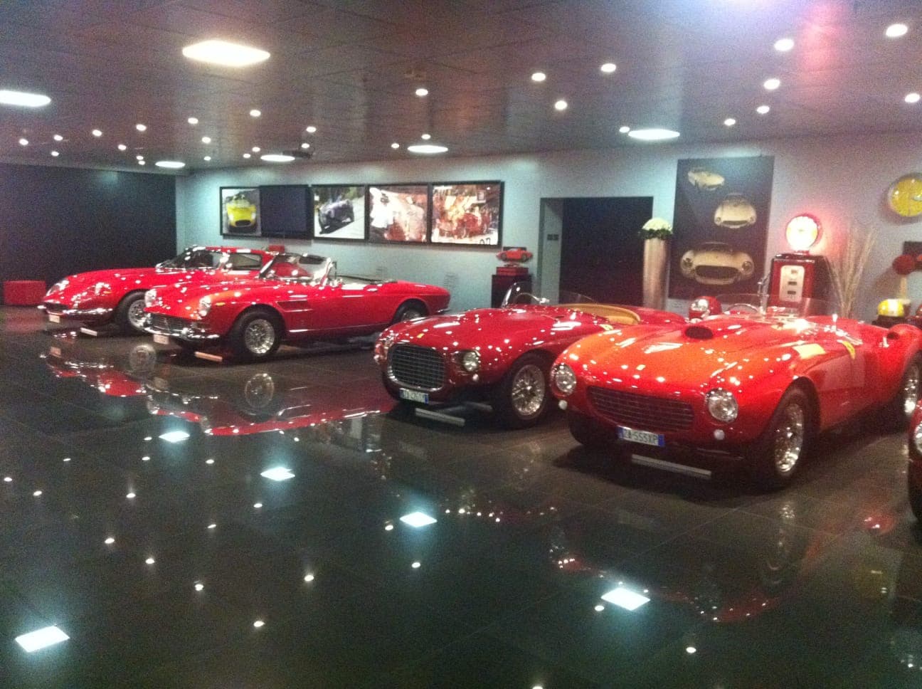 Four classic red Ferraris displayed on a reflective black floor in a showroom.